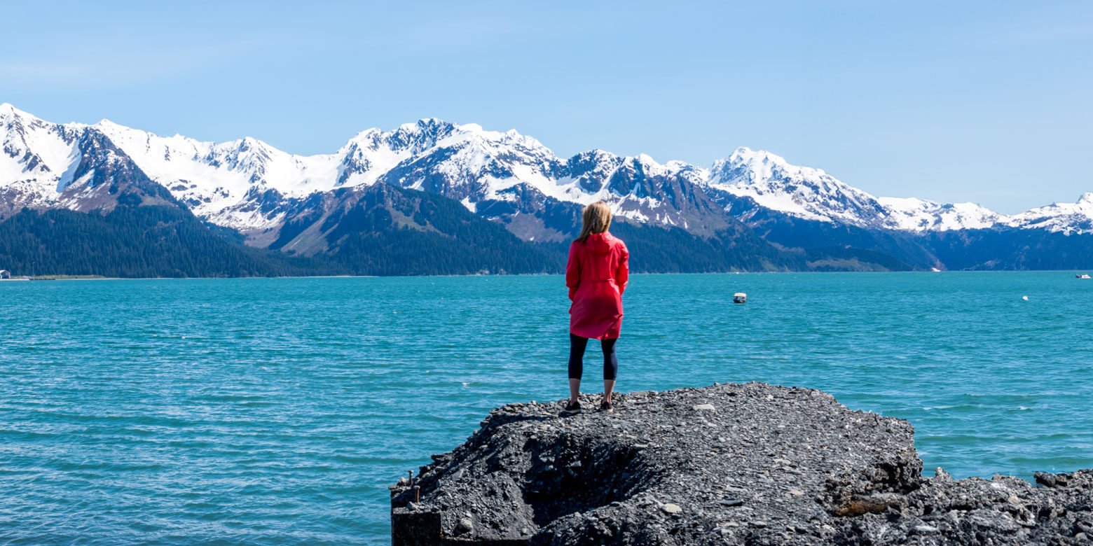 Woman standing on a rock overlooking snow cap mountains