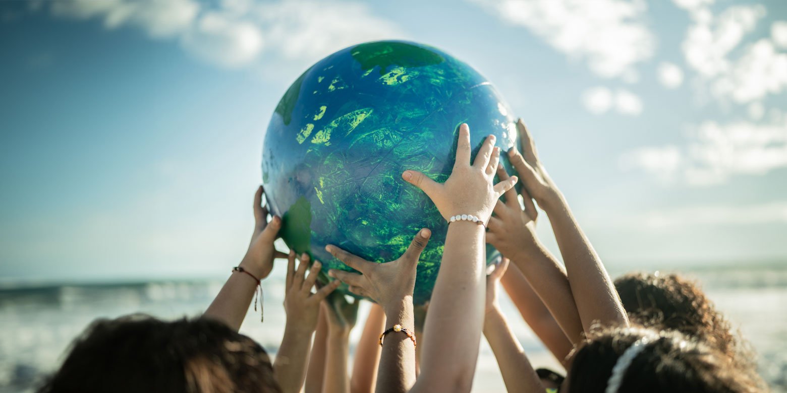 Group of hands working together to hold up a big ball resembling earth