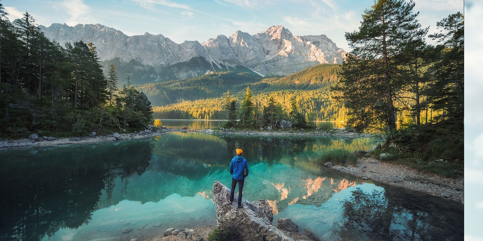 Man standing on rocks looking at peaceful lake and mountains