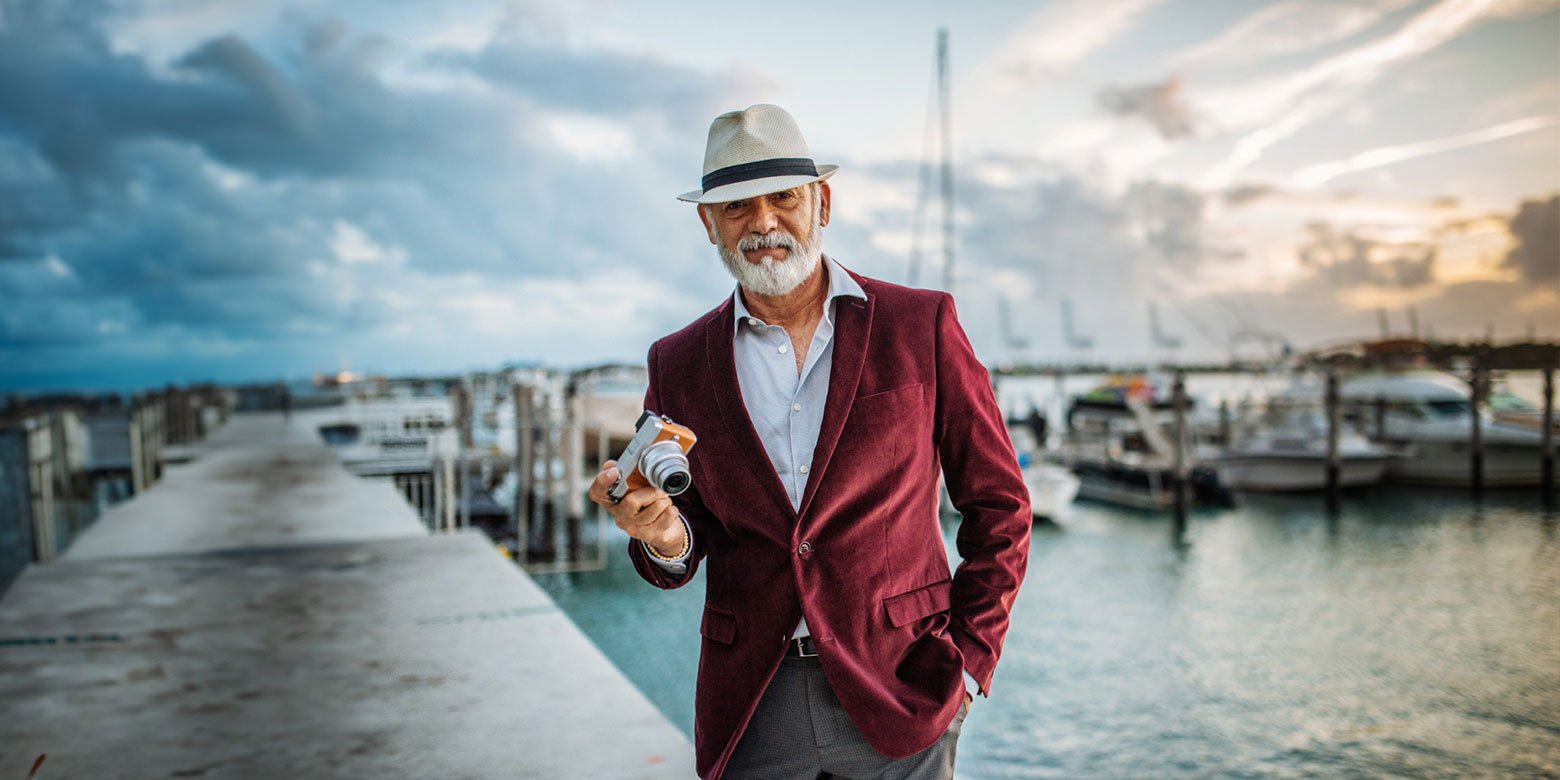 Man with a camera stands in front of a dock with boats