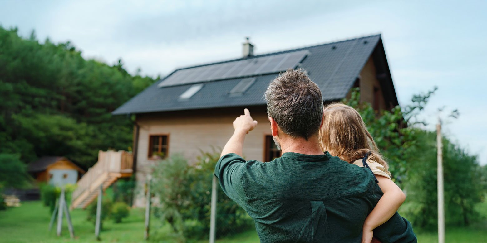 Father holding young daughter pointing at rooftop solar panels