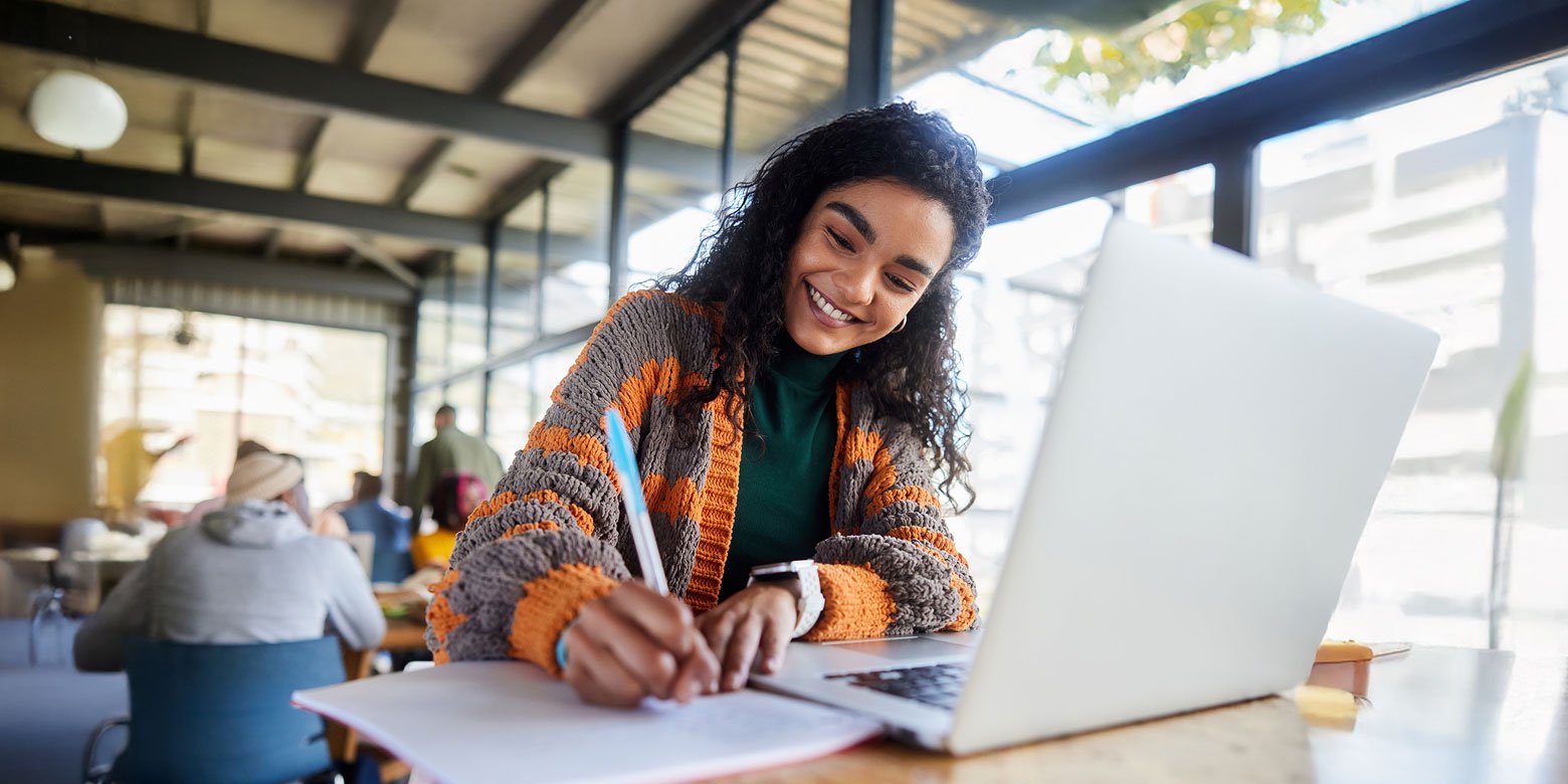 Student taking notes and working on a laptop