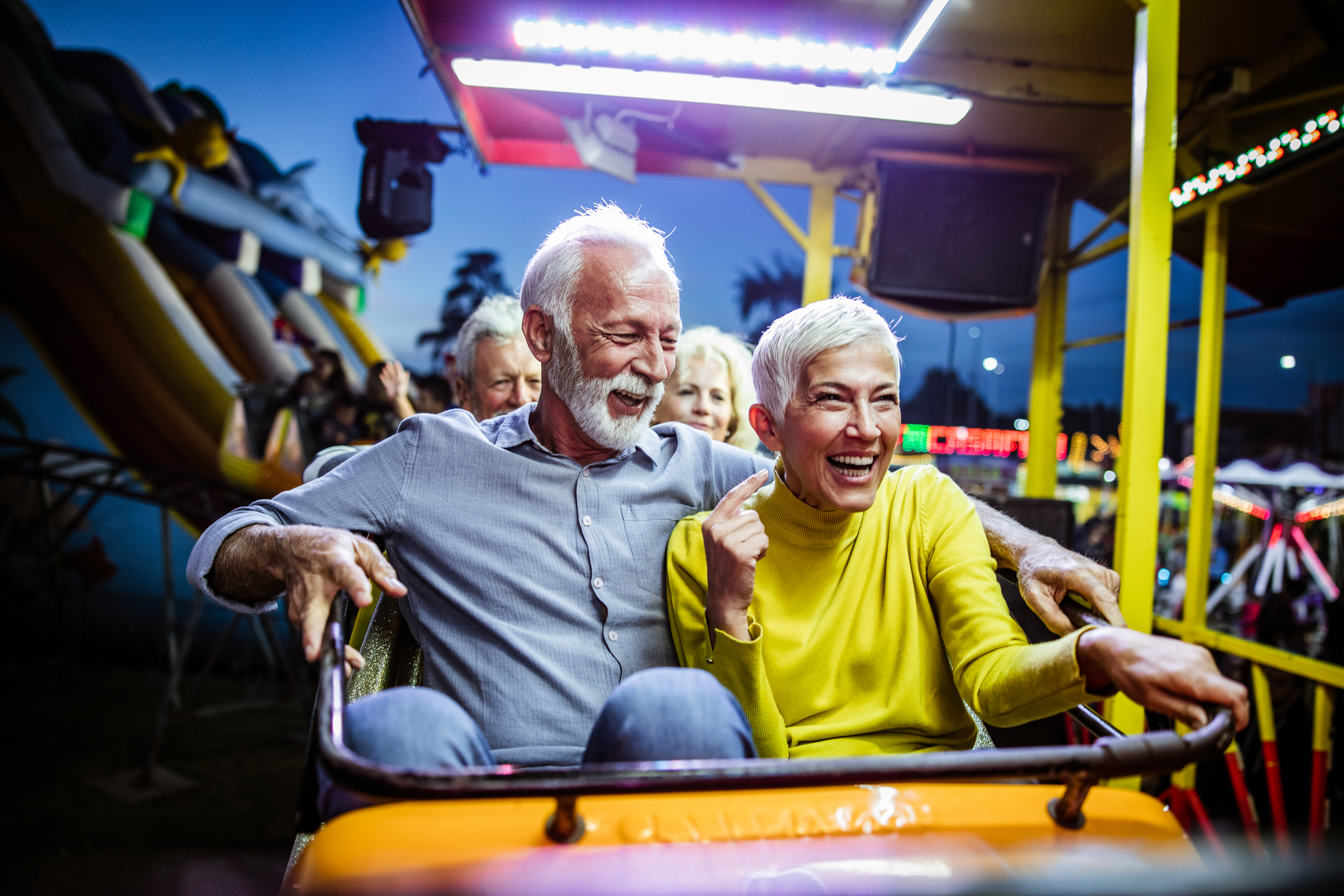 A mature couple sits in a roller-coaster car, ready to ride.
