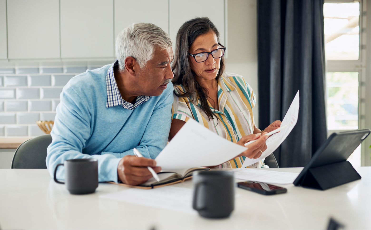 A mixed-race couple leans into one another as they go over paperwork at the kitchen table