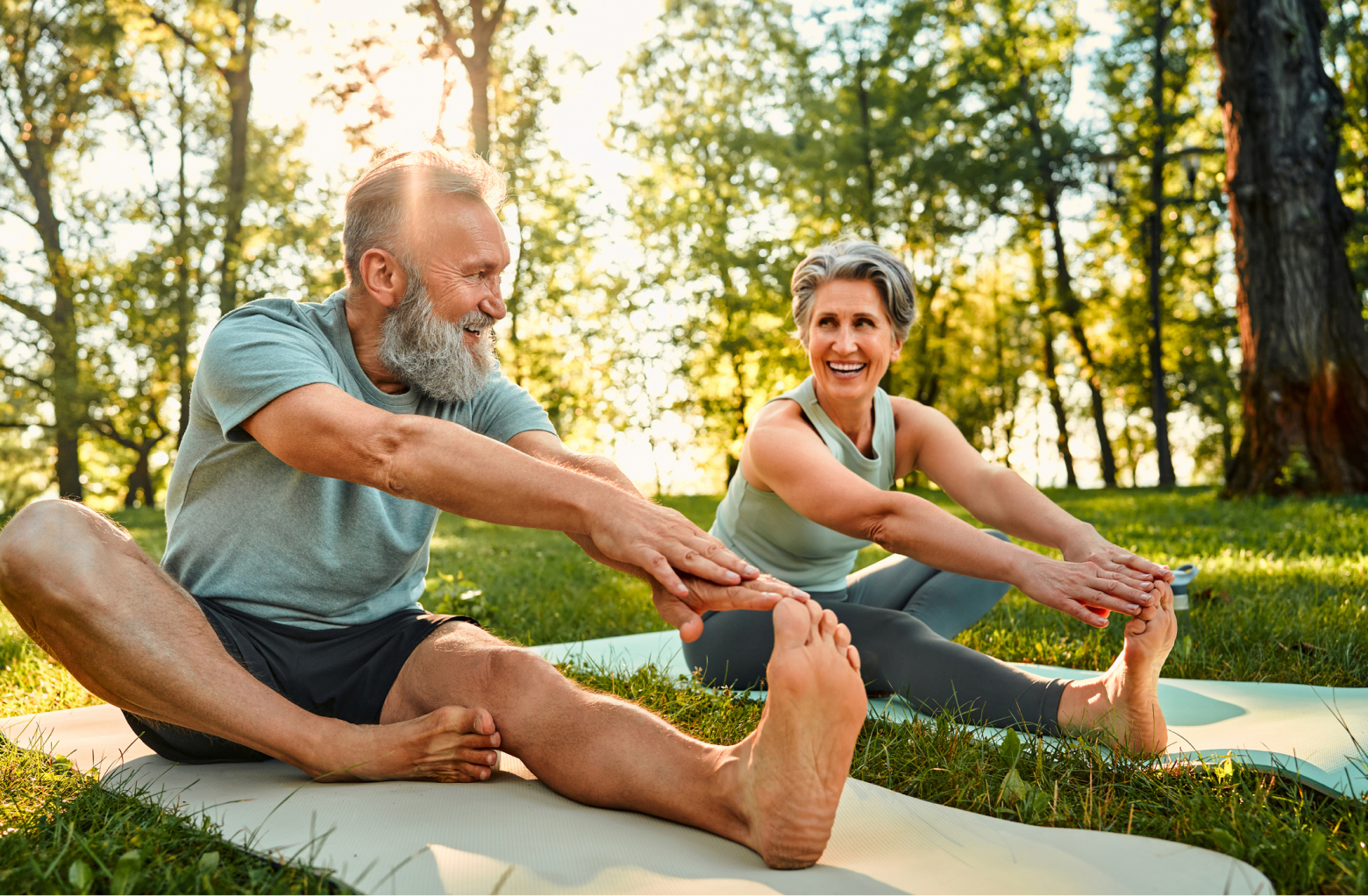 A mature couple stretches on matching yoga mats under the trees