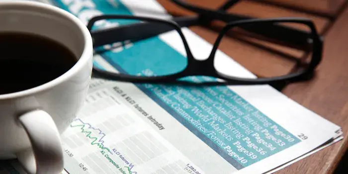 financial newspaper with coffee mug and spectacles sitting on top of it investing markets media finance email-1
